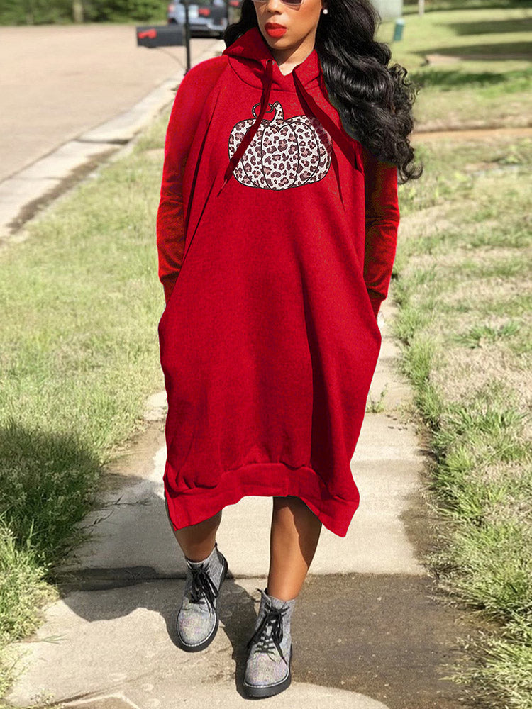 Woman wearing a red hooded midi dress with a pumpkin graphic print and leopard pattern, standing outdoors.