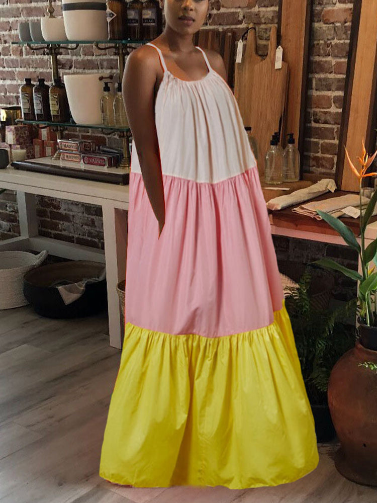 Woman modeling a flowing, tiered maxi dress with spaghetti straps. The dress is color-blocked with light pink, pastel pink, and yellow fabric and is shown in a retail setting.
