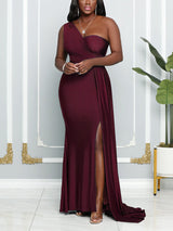 Woman wearing a floor-length, one-shoulder burgundy dress with a high leg slit and draped detailing.