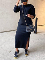 Woman in a long black hooded dress with side slits, sunglasses, and sneakers.