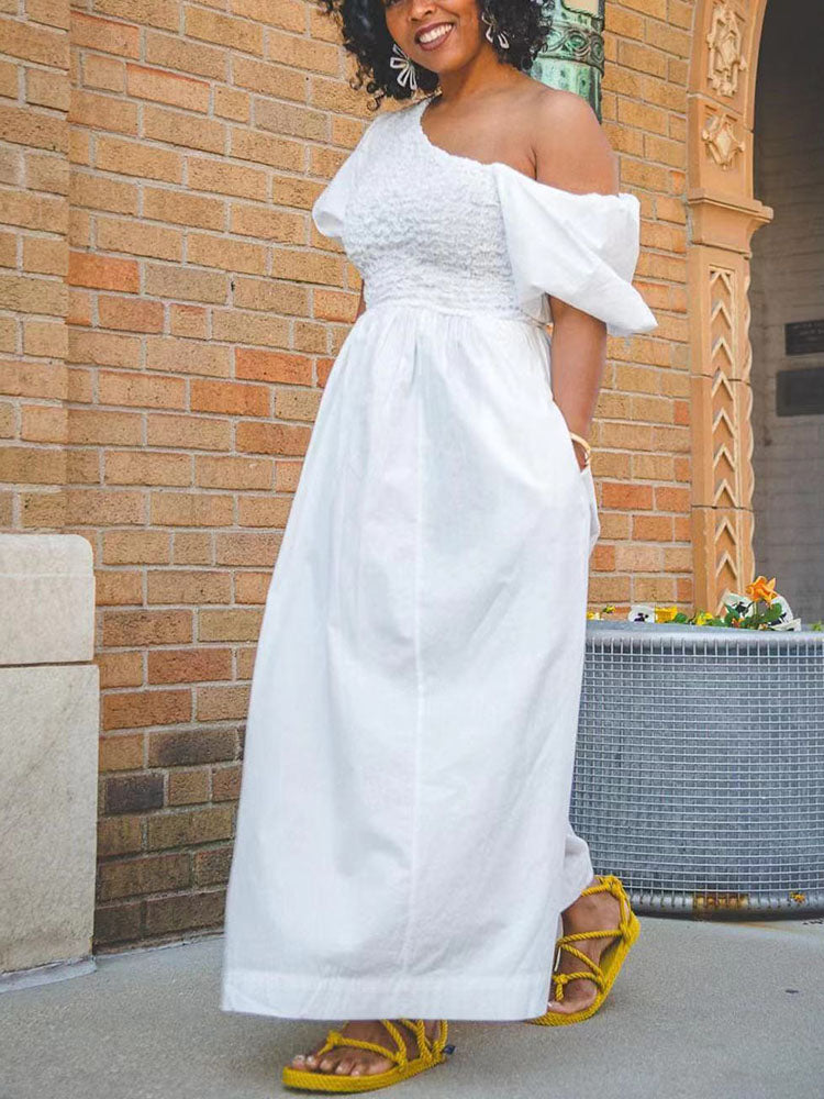Close-up of a woman in a white one-shoulder maxi dress, showing the smocked bodice and cut-out detail.