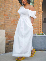 Close-up of a woman in a white one-shoulder maxi dress, showing the smocked bodice and cut-out detail.