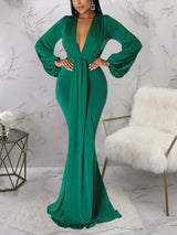 Woman in an emerald green formal gown with draped detailing and a mermaid hemline.