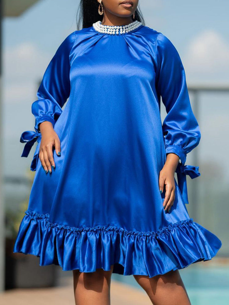 Woman wearing a royal blue satin A-line dress with ruffled hem and pearl-embellished neckline.