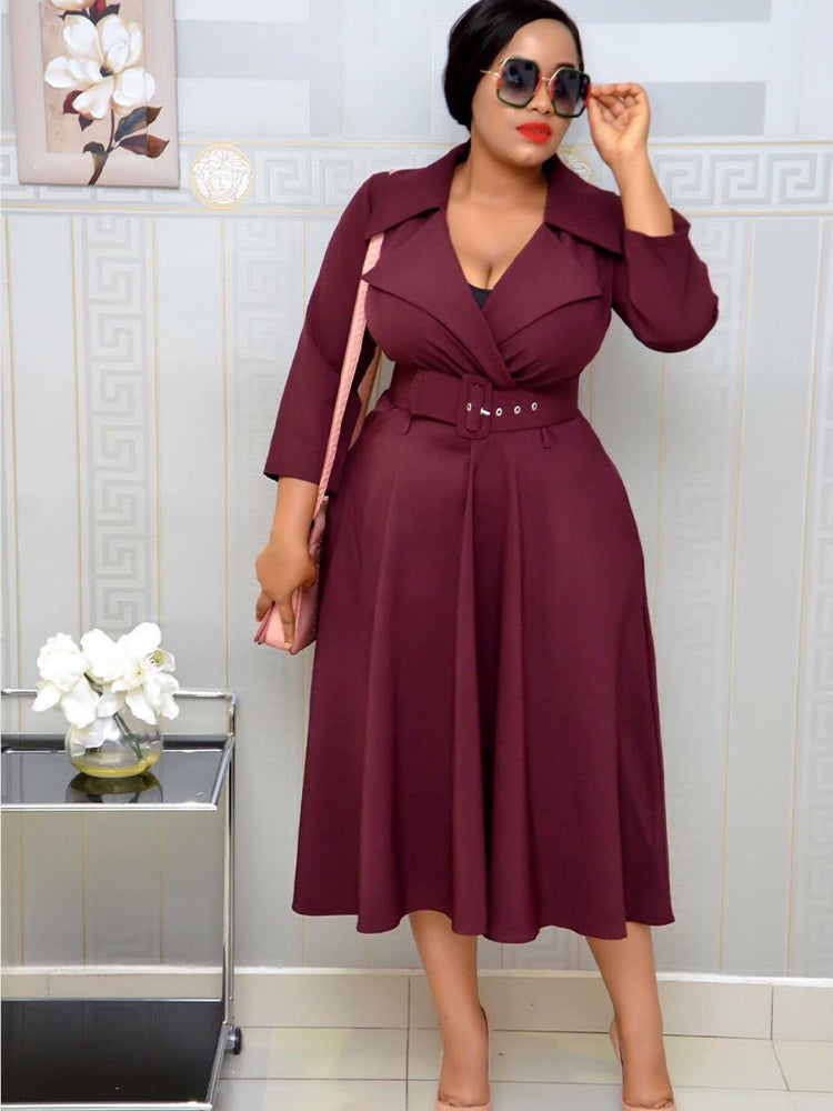 Woman in a burgundy fit and flare dress with a belted waist, lapel collar, and sunglasses, carrying a pink crossbody bag.