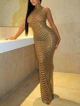 Woman wearing a long, gold beaded, sheer halter neck gown, leaning against a counter.