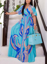Woman wearing a blue and pink abstract print maxi dress with flutter sleeves and a V-neckline, holding a light blue handbag.