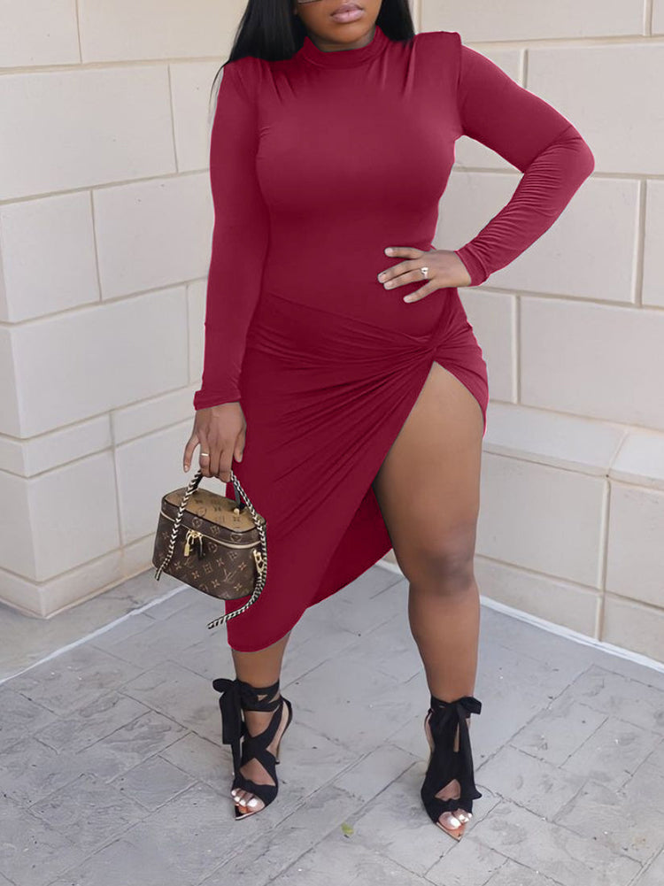 Woman wearing a long-sleeved, high-neck, draped red midi dress with a high slit, posing outdoors with a handbag.