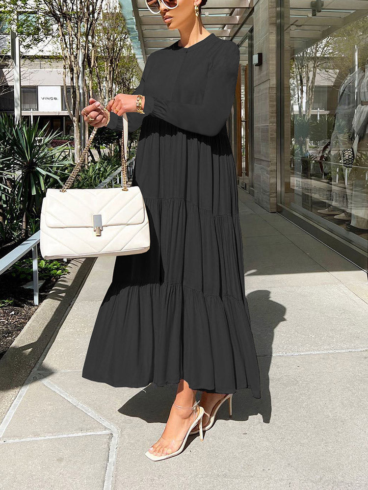 Woman holding a white quilted handbag while wearing a long, black tiered maxi dress with long sleeves.