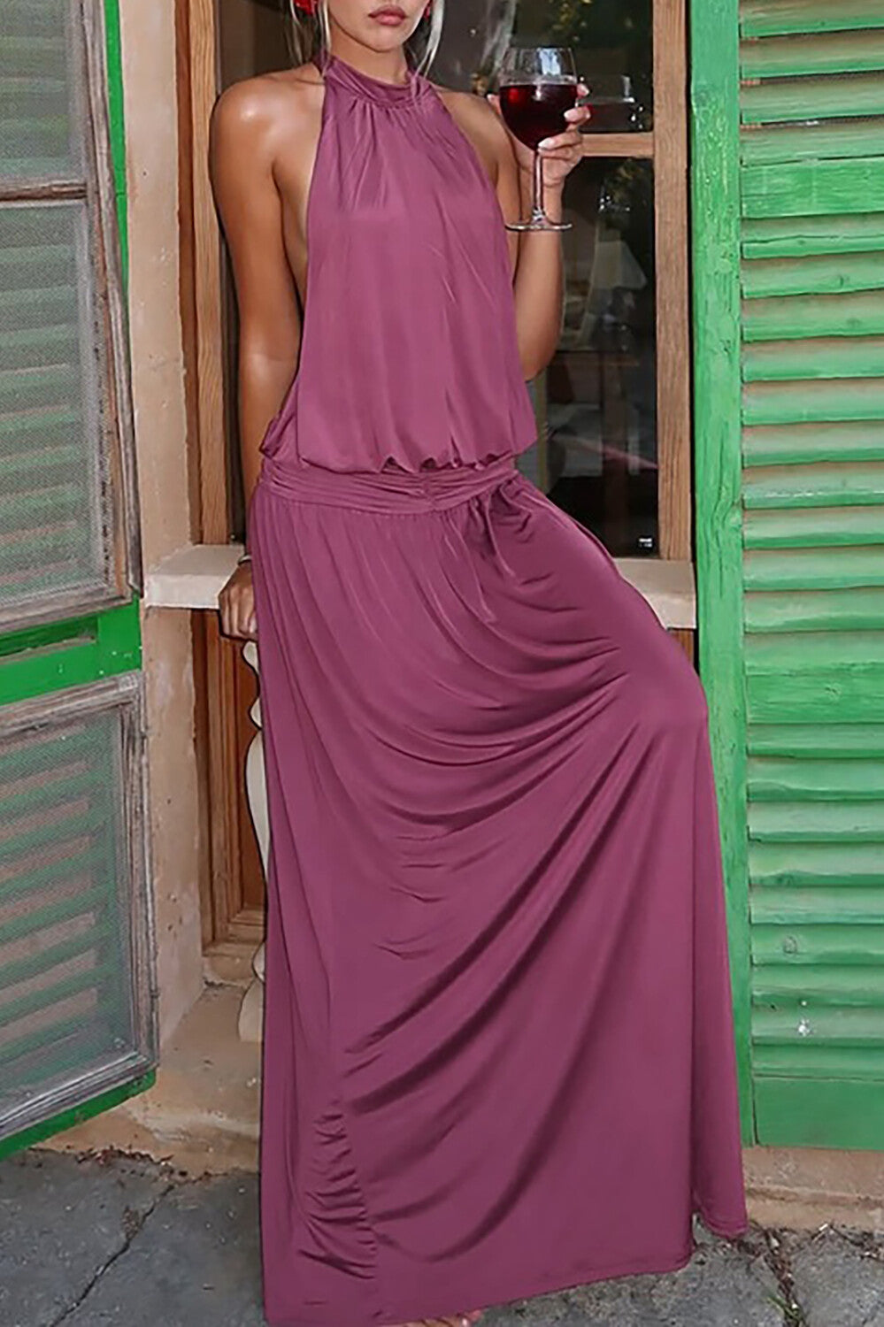 woman wearing a plum halter neck maxi dress leaning against a window frame