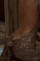 Close-up of the lower back of a woman wearing a gold sequined long-sleeved mini dress, showing a tattoo.