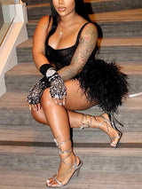 Woman in a black mini dress with feather trim, wearing strappy heels, posing on stairs.