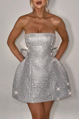Woman wearing a sparkling silver strapless A-line mini dress with a large bow detail on the back and pockets.
