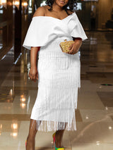 Woman in a white off-the-shoulder dress with a tiered fringe skirt and a gold clutch, posing.