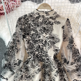 Detail shot of the sequin and lace trim on the mock neck of a black and white floral embroidered midi dress.