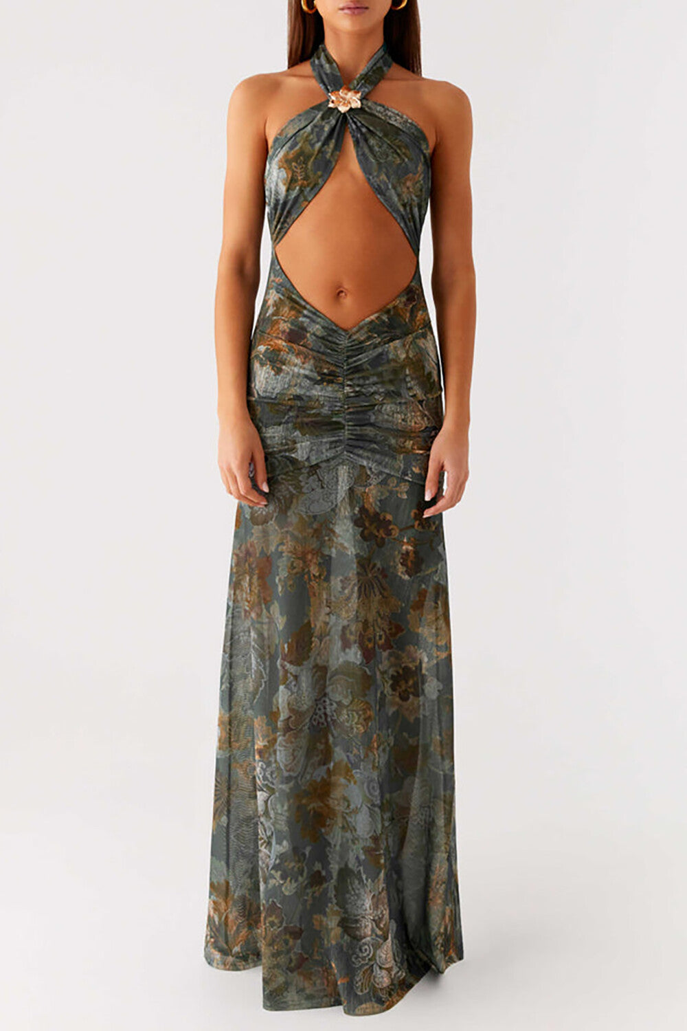 Woman wearing a teal and brown floral print halter neck maxi dress with a cut-out at the midriff, standing against a white wall.