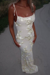 Close-up of a woman wearing a fitted cream dress with floral appliqué and spaghetti straps.