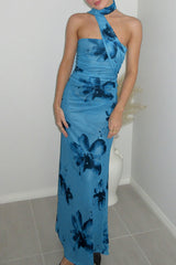 A woman stands in a room wearing a blue floral halter neck maxi dress.