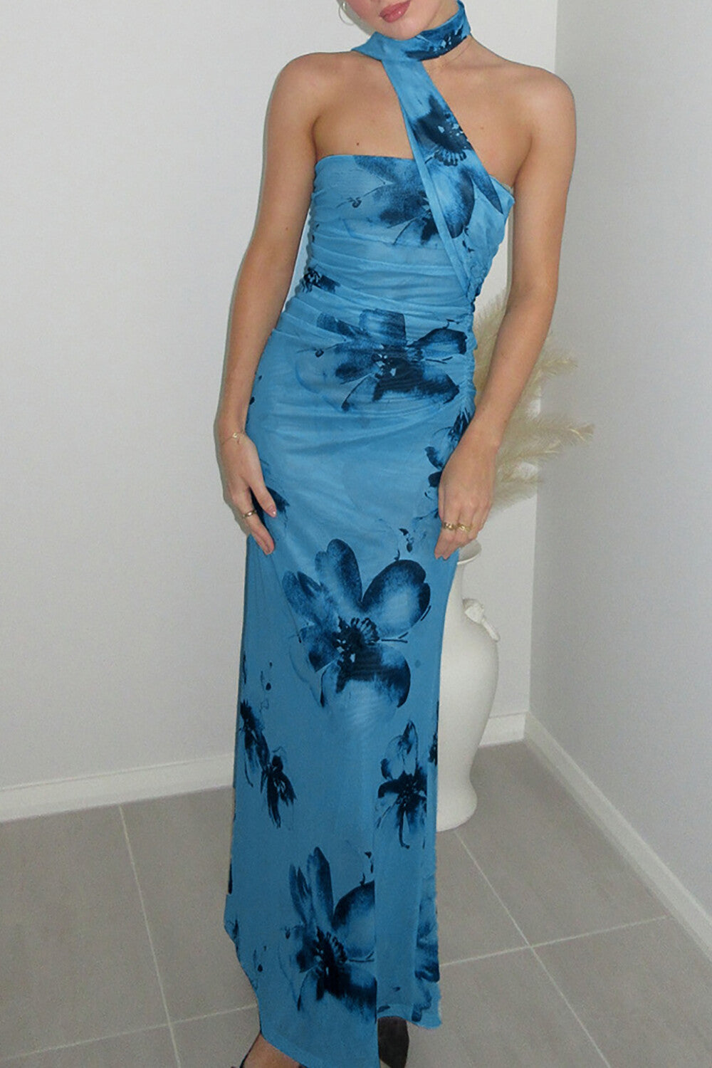 A woman stands in a room wearing a blue floral halter neck maxi dress.