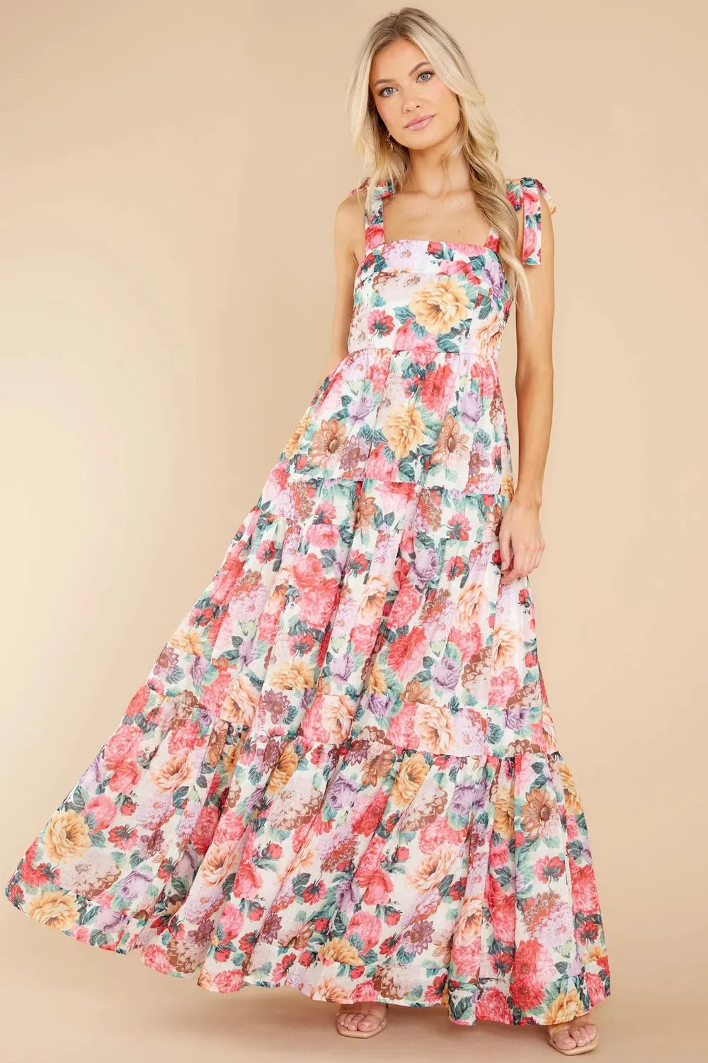Model posing in a long floral dress with a square neckline and tie shoulder details.
