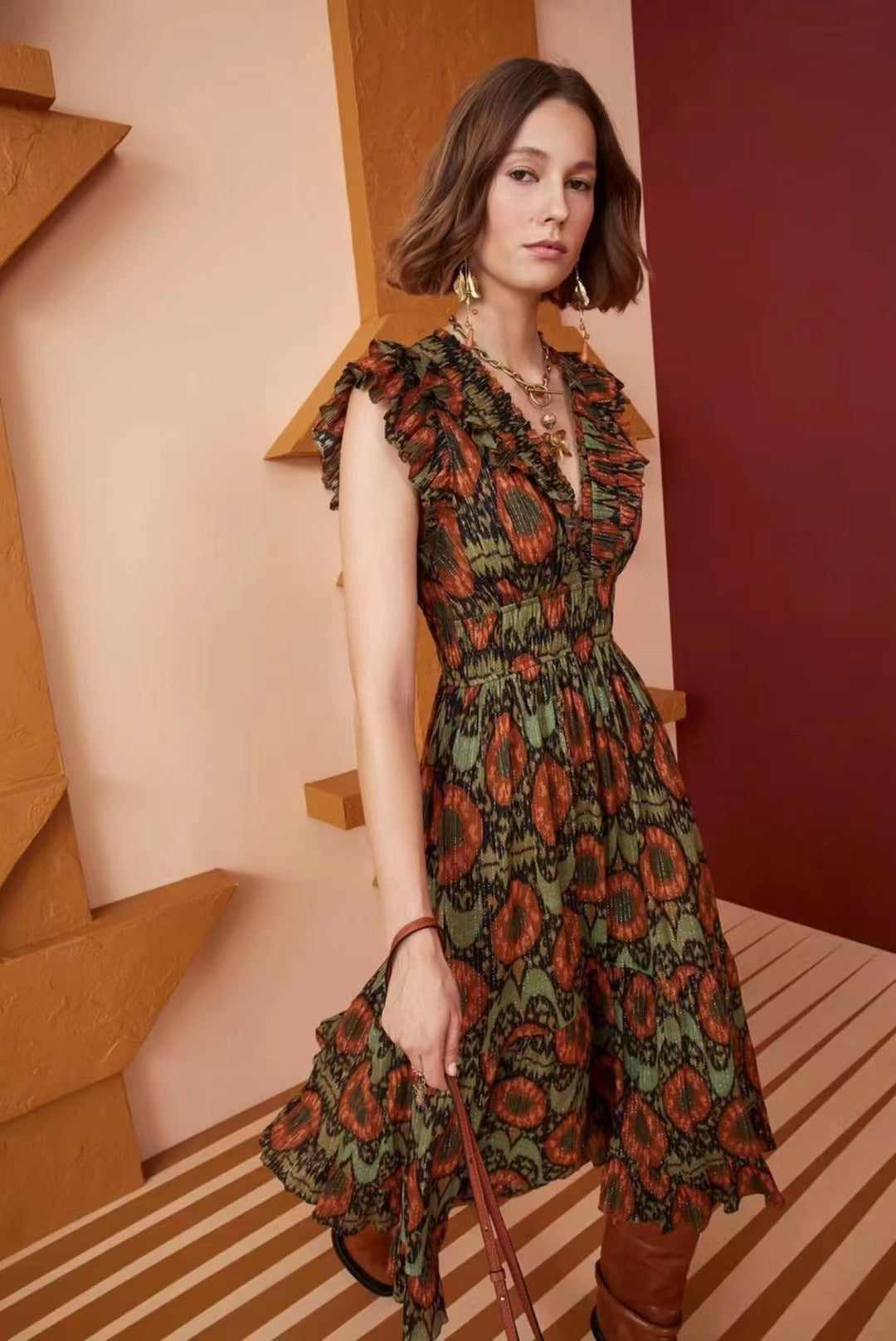Woman wearing a green and orange patterned metallic jacquard midi dress with ruffled sleeves and a V-neckline.
