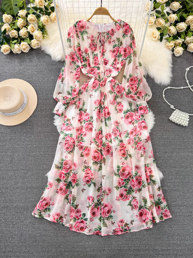 A full-length view of a white chiffon maxi dress with a pink floral print, featuring cut-out details at the waist and long puff sleeves.