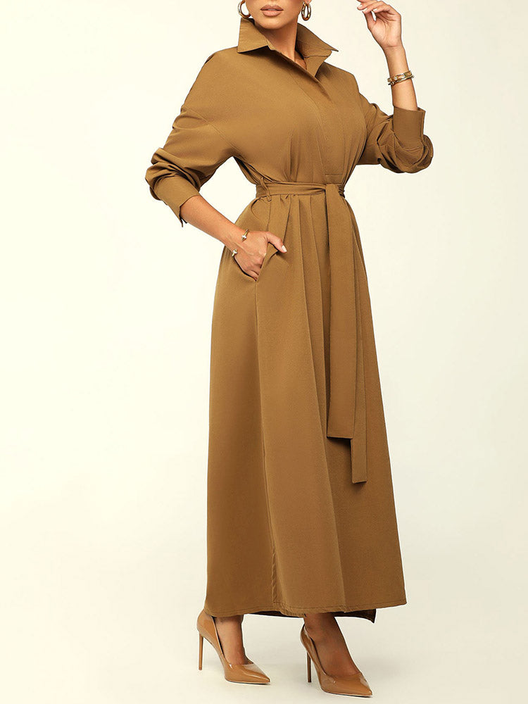 Woman wearing a long brown collared dress with a belted waist, showing pockets, and brown high heels.