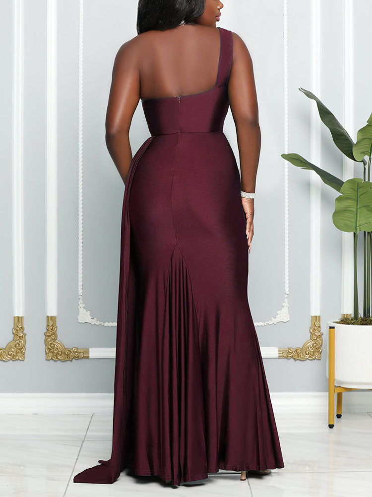 Back view of a woman wearing a floor-length, one-shoulder burgundy dress with a high leg slit and pleated detail.