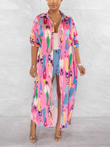 Woman wearing a long, pink collared shirt dress with a colorful graphic print of people, open over denim shorts.