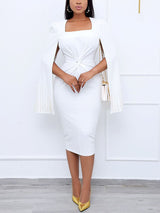 Woman wearing a white knee-length dress with cape sleeves and a square neckline.