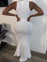 Back view of a woman wearing a white sleeveless ribbed knit maxi dress with a mermaid hem and mock neckline.