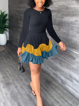Woman wearing a black long-sleeved dress with a tiered, ruffled hem in shades of yellow and blue.