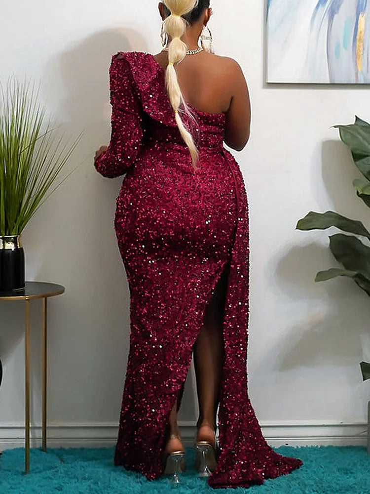 Back view of a woman in a floor-length, one-shoulder, sequined gown with a high slit in red, showing the train.