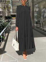 Woman wearing a long, black tiered maxi dress with long sleeves and a white handbag.