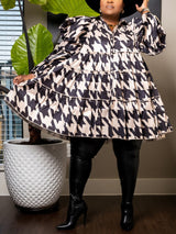 Woman in a black and white houndstooth print mini dress with puffed sleeves and a tiered skirt, paired with black boots.