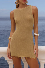 Woman wearing a gold knit mini dress with a round neckline and sleeveless design, standing outdoors by the ocean.