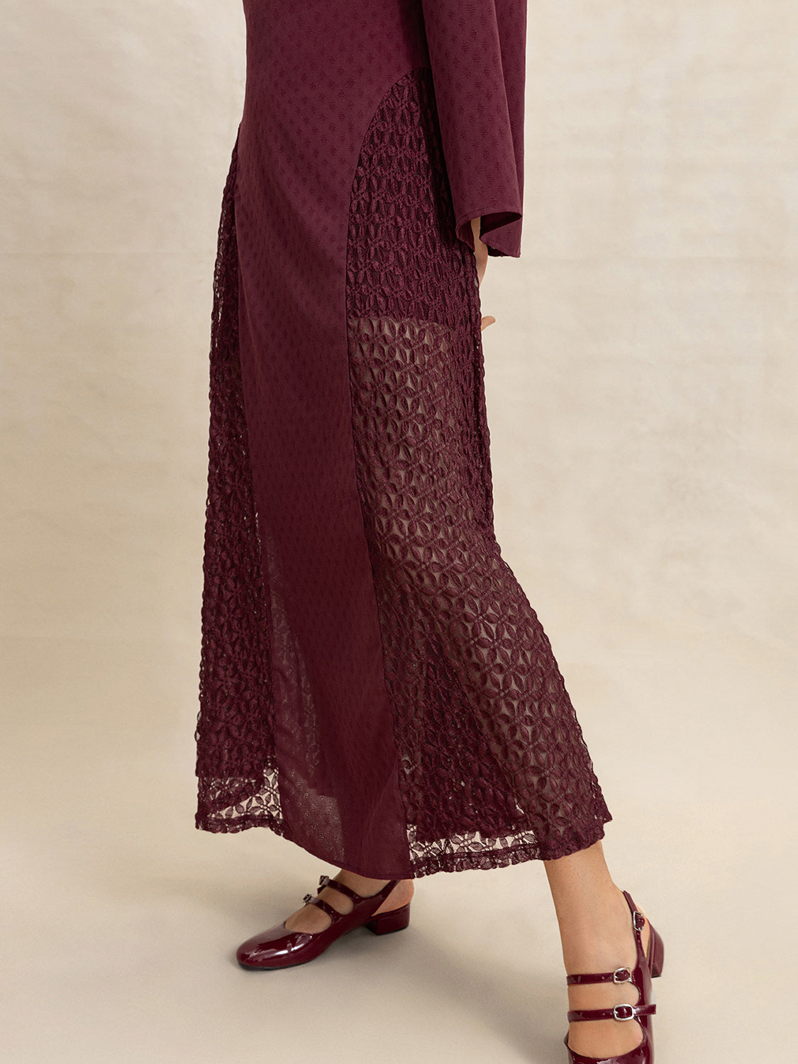 Detail shot of the lace inserts and textured fabric of a burgundy maxi dress.