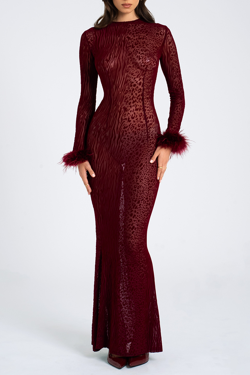 Front studio shot of a woman wearing a long, form-fitting, sheer mesh dress with a mock neck, long sleeves, and feather trim at the cuffs. The dress features an all-over burnout animal print.