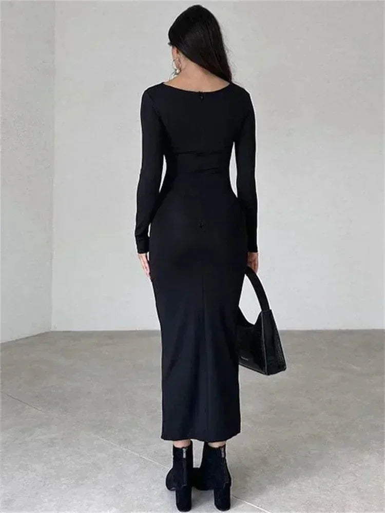 Back view of a woman wearing a long-sleeved, ruched, black maxi dress and black ankle boots.