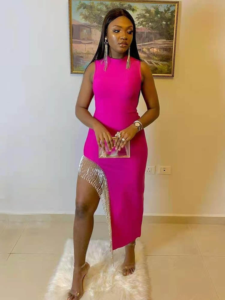 Woman in a bright pink sleeveless mock neck dress with an asymmetrical hemline and embellished trim, accessorized with long earrings and a clear clutch.