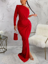 Woman wearing a red one-shoulder long sleeve ruched maxi dress with a high slit, holding a red beaded clutch.