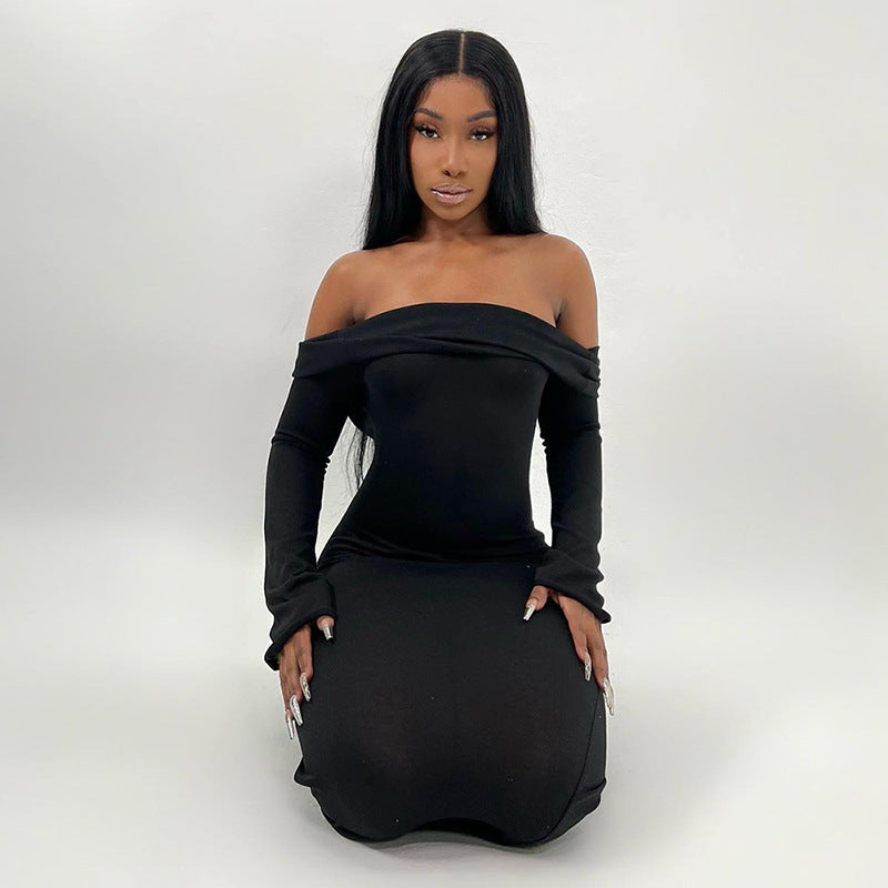 Woman wearing a long black off-the-shoulder dress with long sleeves, kneeling on a white floor.