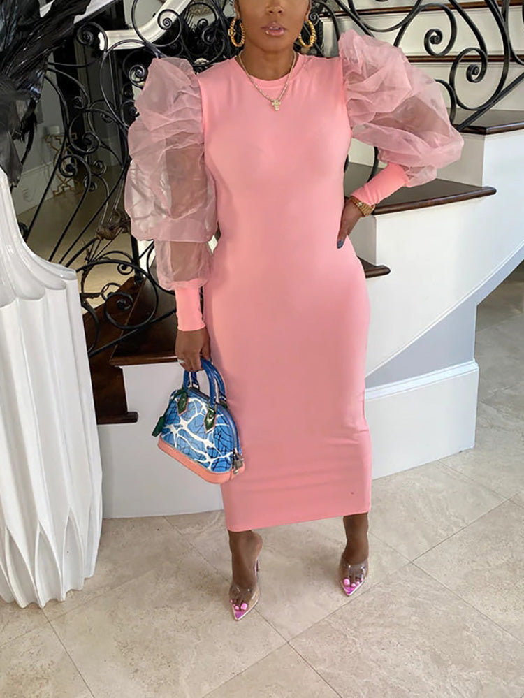 Woman in a pink dress with sheer puff sleeves and a handbag by a staircase