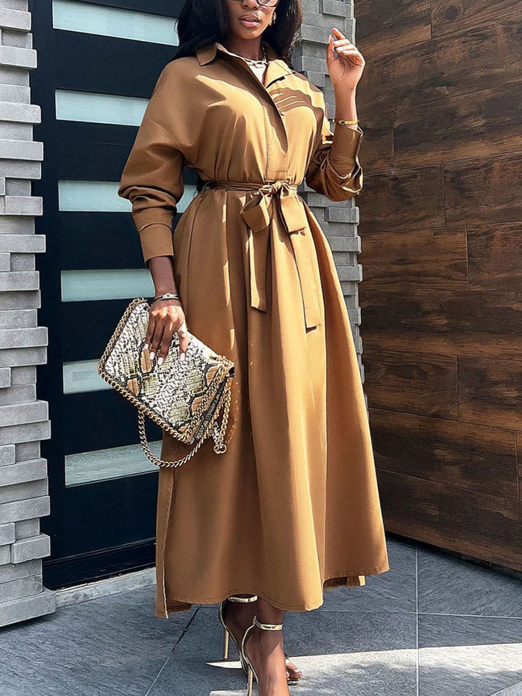 Woman wearing a long brown collared dress with a belted waist and a snakeskin clutch.