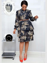 Woman in a black paisley print tiered dress, brown belt, and red heels, with a black handbag.