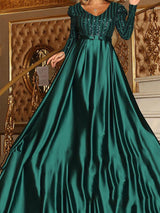 Woman wearing a green long-sleeved A-line formal dress with a sequined bodice and a satin skirt.