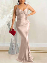 Woman wearing a long champagne satin dress with spaghetti straps and a plunging neckline, holding a red clutch.