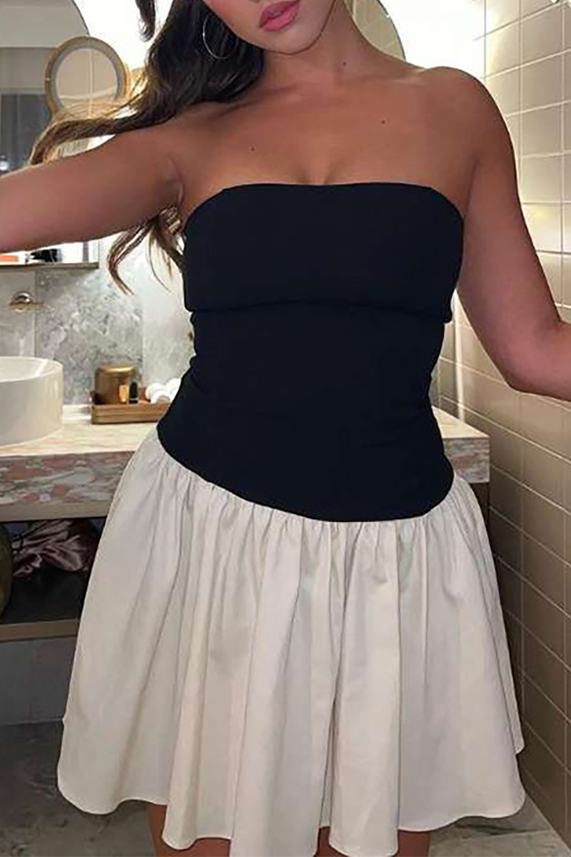 Close-up of a woman wearing a black strapless top and cream pleated mini skirt in a bathroom setting.