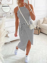 Woman modeling a black and white striped halter neck dress with a tie waist and side slit, styled with white sneakers and a white crossbody bag.