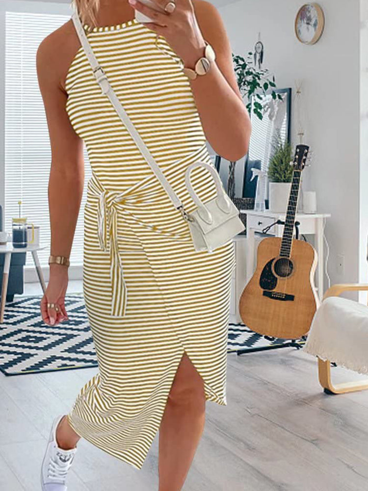 Woman wearing a yellow and white striped halter neck dress with a tie waist and side slit, paired with white sneakers and a white crossbody bag.
